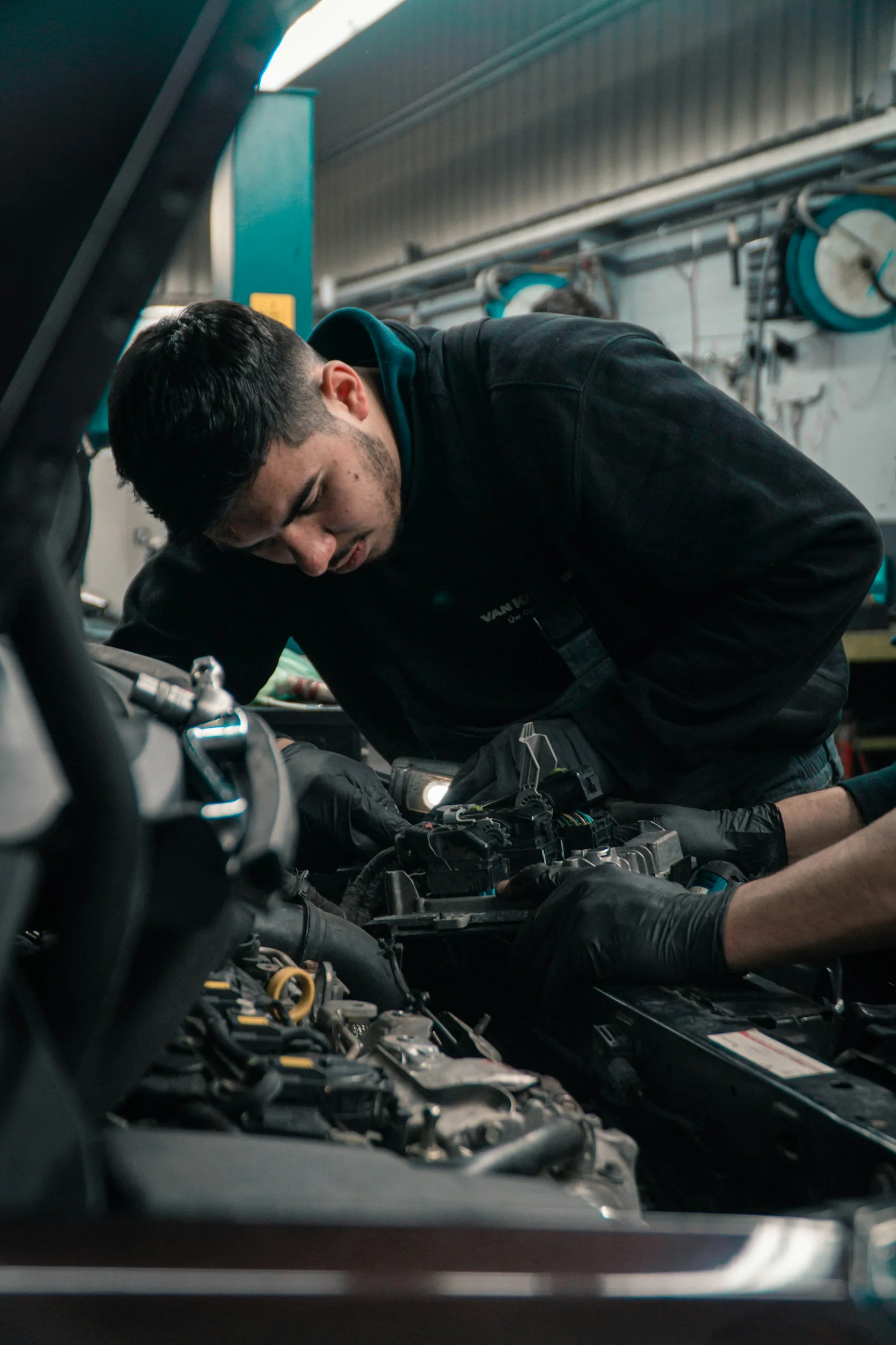 Mechanic working under the hood of a car in a repair bay