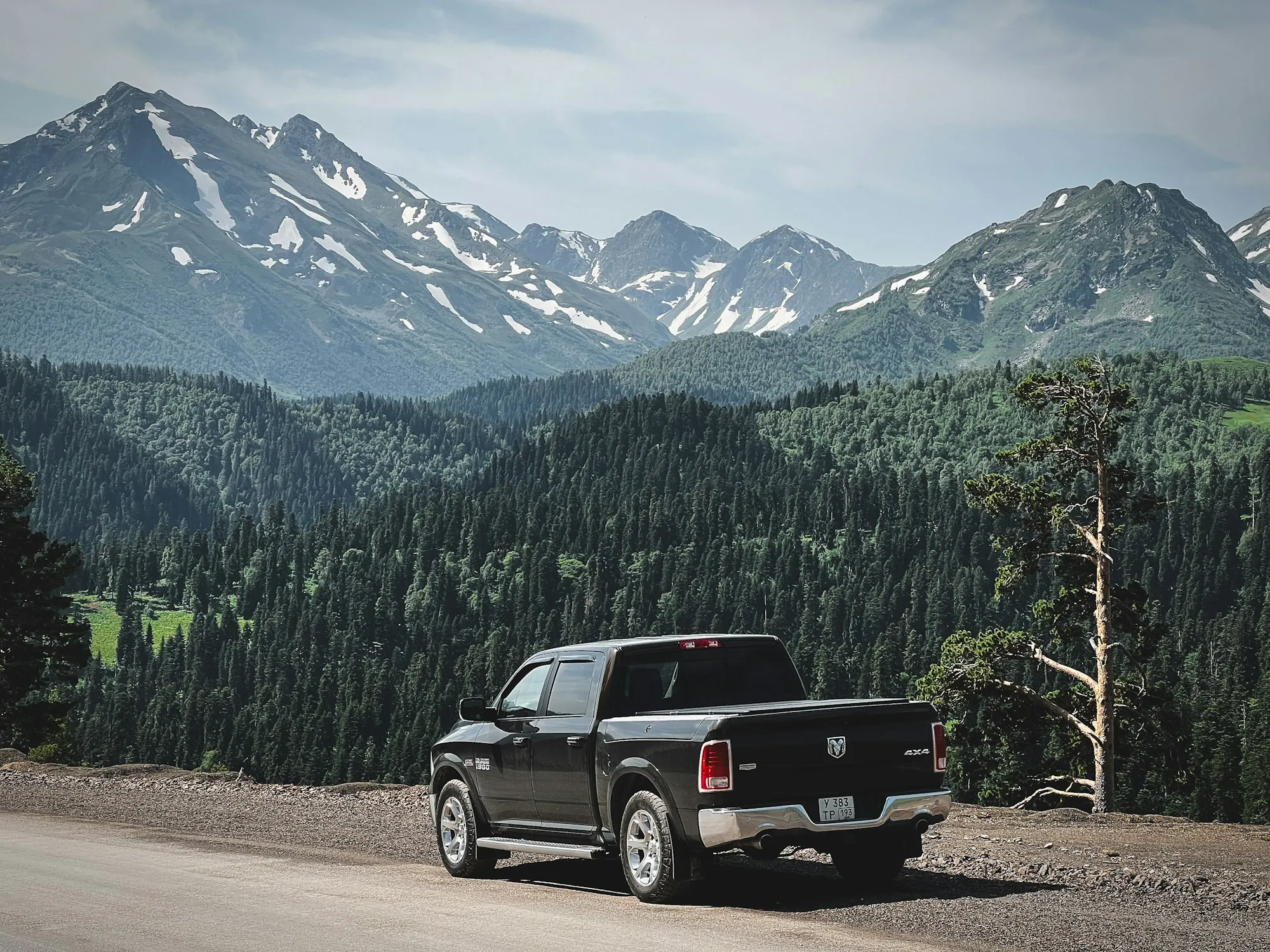 Dark pickup truck parked on a road below snowy mountain peaks